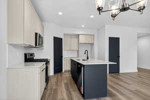 Kitchen with light stone counters, stainless steel appliances, modern cabinets, a chandelier, and light brown cabinets