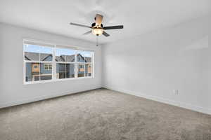 Empty room featuring carpet flooring, ceiling fan, and a residential view