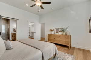 Bedroom with a barn door, light wood-type flooring, a walk in closet, ceiling fan, and ensuite bathroom