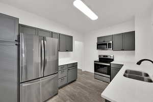 Kitchen with gray cabinets, stainless steel appliances, light wood finished floors, and light stone countertops
