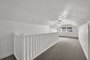 Bonus room featuring carpet flooring, vaulted ceiling, and a textured ceiling