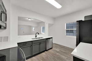 Kitchen with stainless steel appliances, gray cabinetry, light wood-style flooring, and light stone countertops