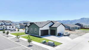 View of front of house with board and batten siding, a residential view, concrete driveway, a front lawn, and a mountain view