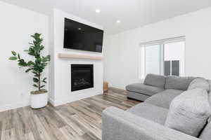 Living area with a glass covered fireplace, wood finished floors, and recessed lighting