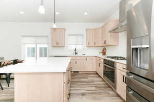 Kitchen featuring light brown cabinets, appliances with stainless steel finishes, a kitchen island, wall chimney exhaust hood, and recessed lighting