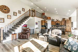 Living area with recessed lighting, stairs, light wood finished floors, and high vaulted ceiling