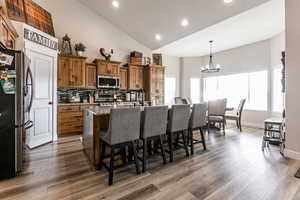 Kitchen with brown cabinets, recessed lighting, appliances with stainless steel finishes, light stone counters, and decorative light fixtures