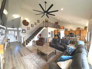 Living room featuring high vaulted ceiling, stairs, light wood-style floors, a ceiling fan, and recessed lighting