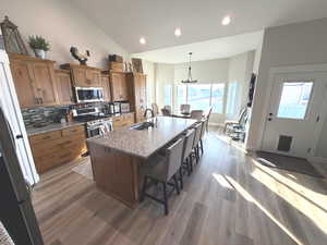 Kitchen featuring brown cabinets, dark stone countertops, a center island with sink, a kitchen breakfast bar, and decorative light fixtures