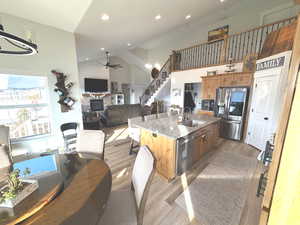 Kitchen with open floor plan, stainless steel appliances, light stone countertops, high vaulted ceiling, and a stone fireplace