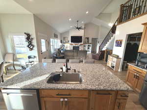 Kitchen with light wood-style floors, brown cabinetry, appliances with stainless steel finishes, dark stone countertops, and high vaulted ceiling