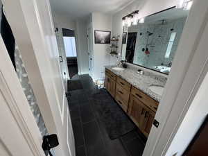 Full bath featuring a shower stall, double vanity, and dark tile patterned floors