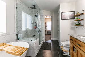 Bathroom featuring a marble finish shower, vanity, a soaking tub, and dark tile patterned floors