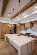 Kitchen with a large island, light wood finished floors, decorative light fixtures, light stone counters, and beamed ceiling