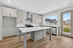 Kitchen featuring appliances with stainless steel finishes, a kitchen bar, wall chimney exhaust hood, modern cabinets, and recessed lighting