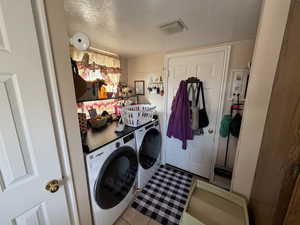 Washroom with a textured ceiling, washing machine and clothes dryer, and light tile patterned flooring