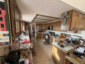 Kitchen featuring brown cabinetry, light tile patterned floors, appliances with stainless steel finishes, light countertops, and a textured ceiling