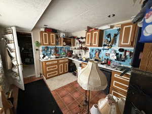 Kitchen with brown cabinetry, a textured ceiling, light countertops, dark tile patterned floors, and open shelves