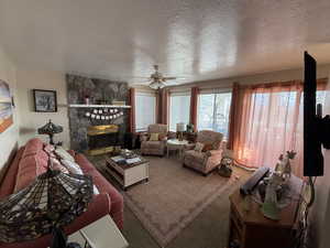 Living area featuring a textured ceiling, a stone fireplace, ceiling fan, and carpet