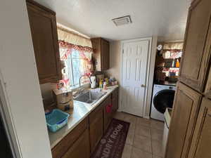Kitchen featuring light countertops, washer / dryer, a textured ceiling, and light tile patterned floors