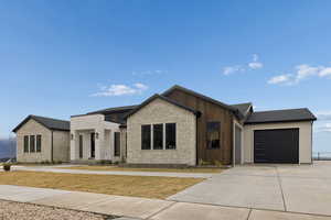 View of front facade featuring an attached garage, concrete driveway, and stone siding