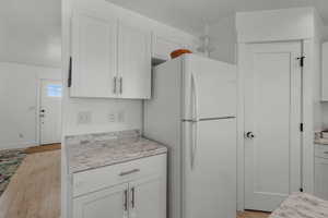 Kitchen with light countertops, freestanding refrigerator, white cabinetry, and light wood finished floors