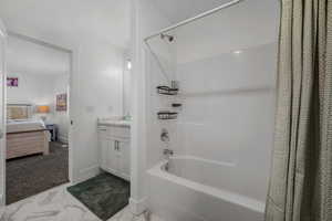 Ensuite bathroom featuring shower / tub combo with curtain, vanity, light marble finish flooring, and light carpet