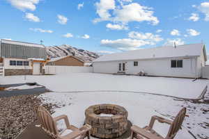 Snow covered back of property with a fire pit, a mountain view, a fenced backyard, and entry steps