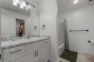 Full bathroom featuring vanity, light marble finish floors, shower / bath combo with shower curtain, and a walk in closet