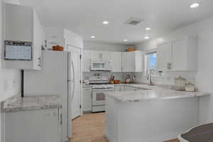 Kitchen with white appliances, light countertops, a peninsula, white cabinets, and light wood finished floors