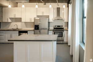 Kitchen with appliances with stainless steel finishes, wall chimney exhaust hood, white cabinets, and a kitchen island