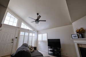 Living room with a ceiling fan, lofted ceiling, a tile fireplace, and carpet flooring