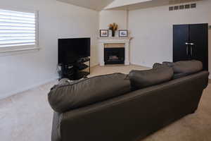 Living area featuring light carpet, a fireplace, and vaulted ceiling