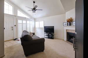 Living room featuring light colored carpet, a fireplace, ceiling fan, high vaulted ceiling, and light tile patterned flooring