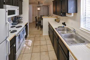 Kitchen with white appliances, light countertops, decorative light fixtures, dark cabinets, and light tile patterned flooring