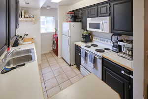 Kitchen with white appliances, light countertops, dark cabinetry, and light tile patterned flooring