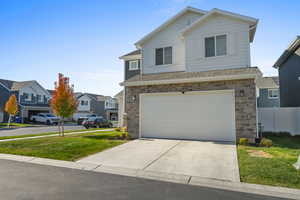 View of front of property featuring driveway, stone siding, an attached garage, and a residential view