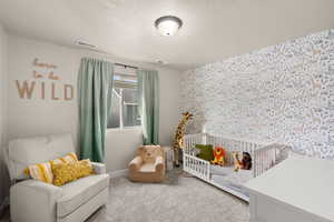 Carpeted bedroom with a textured ceiling, an accent wall, and a crib