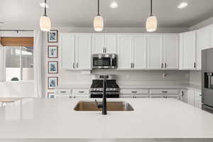 Kitchen with pendant lighting, stainless steel appliances, white cabinetry, light stone countertops, and recessed lighting