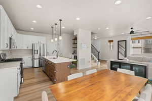 Kitchen with appliances with stainless steel finishes, white cabinetry, a kitchen bar, pendant lighting, and a kitchen island with sink