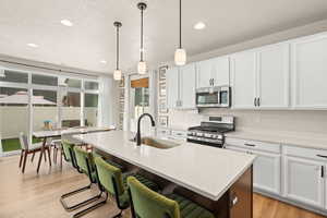 Kitchen featuring white cabinetry, a textured ceiling, appliances with stainless steel finishes, light stone countertops, and light wood finished floors