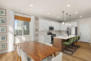 Kitchen with white cabinets, a kitchen bar, stainless steel appliances, an island with sink, and recessed lighting
