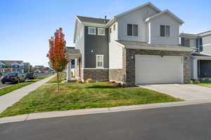 View of front of house with a front lawn, stone siding, driveway, a garage, and a residential view