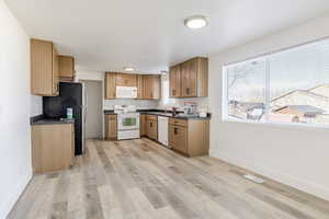 Kitchen featuring dark countertops, white appliances, tasteful backsplash, and light wood-type flooring