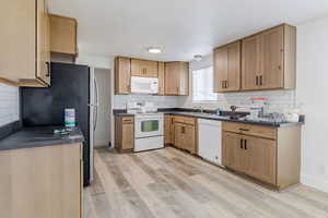 Kitchen featuring white appliances, dark countertops, light brown cabinetry, and light wood-style flooring