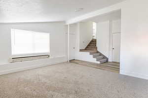 Basement with carpet, stairway, a textured ceiling, and baseboard heating