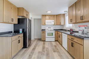 Kitchen with white appliances, light brown cabinets, light wood-style floors, and decorative backsplash