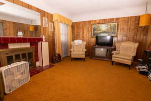 Living area featuring a tile fireplace, wooden walls, heating unit, a textured ceiling, and carpet
