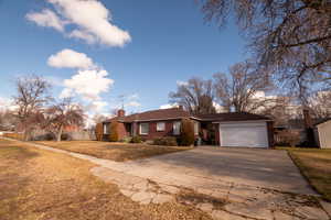 Single story home featuring brick siding, a front lawn, a chimney, concrete driveway, and an attached garage