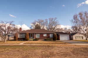 Ranch-style home with driveway, a front lawn, a chimney, brick siding, and a garage
